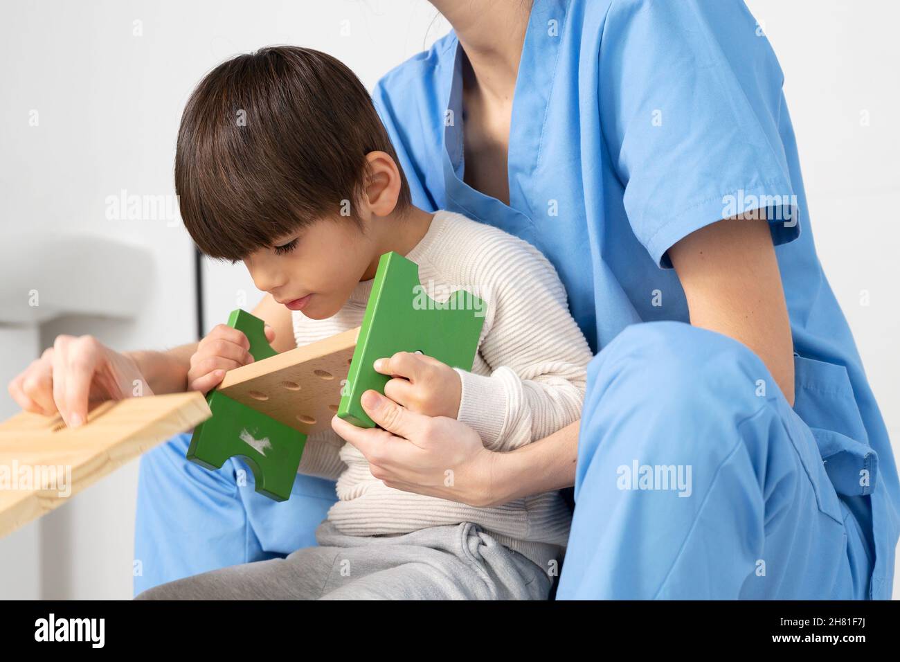 cute kid with disability playing with developing toys while is being helped by physiotherapist in rehabilitation hospital. High quality photo Stock Photo