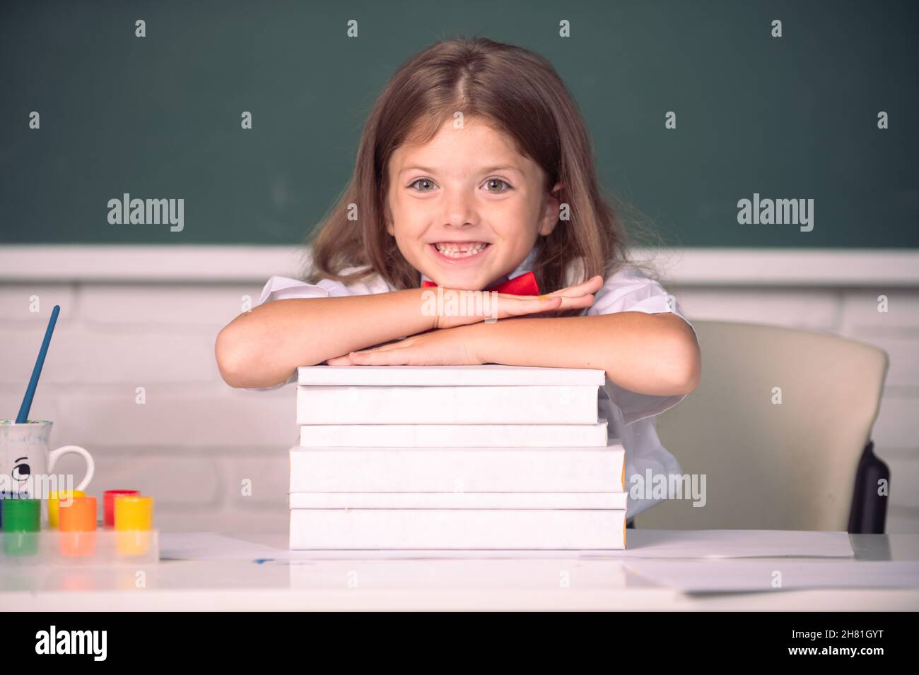 Smiling girl sitting at the desk and holding hands on the books in the ...