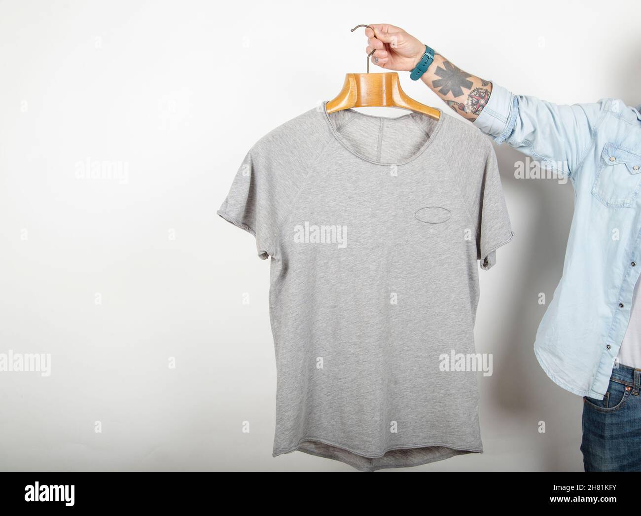 https://c8.alamy.com/comp/2H81KFY/tattooed-male-hand-holds-a-hanger-with-premium-quality-fine-cotton-gray-t-shirt-on-a-white-background-mockup-2H81KFY.jpg