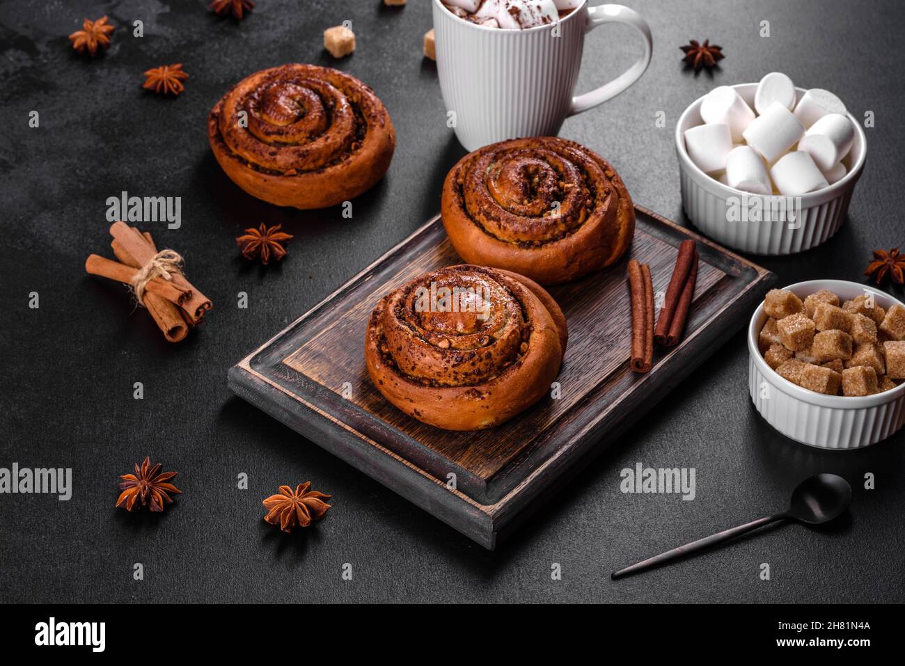 Freshly baked cinnamon roll with spices and cocoa filling on a black background. Cinnabon buns. Swedish breakfast. Stock Photo