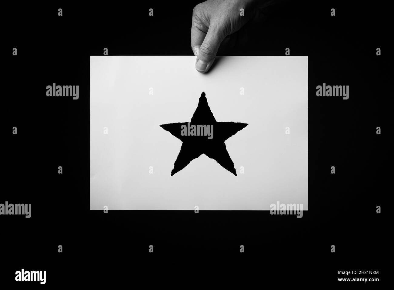 B+W image of male hand holding sheet of paper with christmas star symbol against black background. Stock Photo