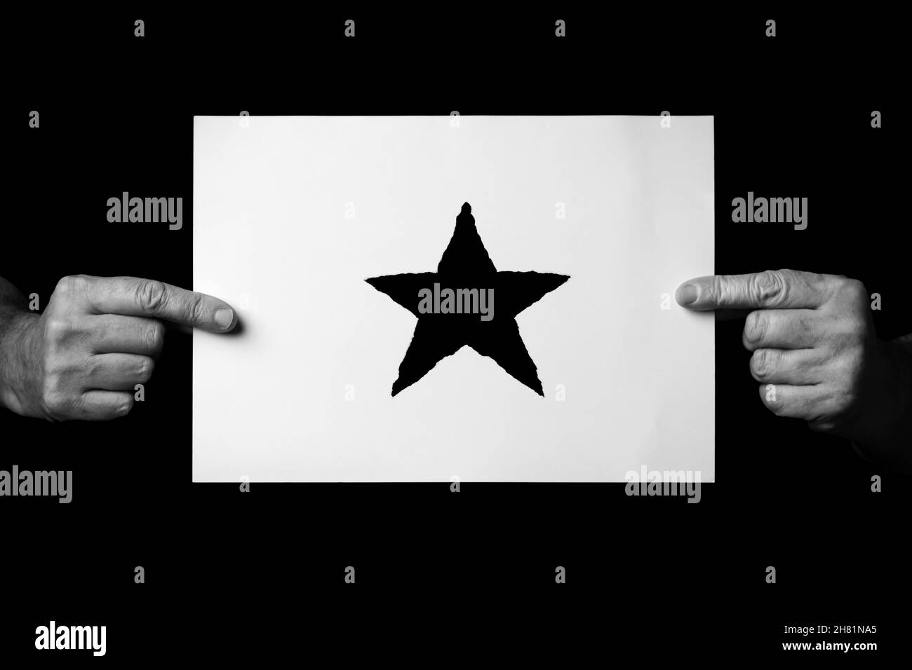 B+W image of male hands holding sheet of paper with christmas star symbol against black background. Stock Photo