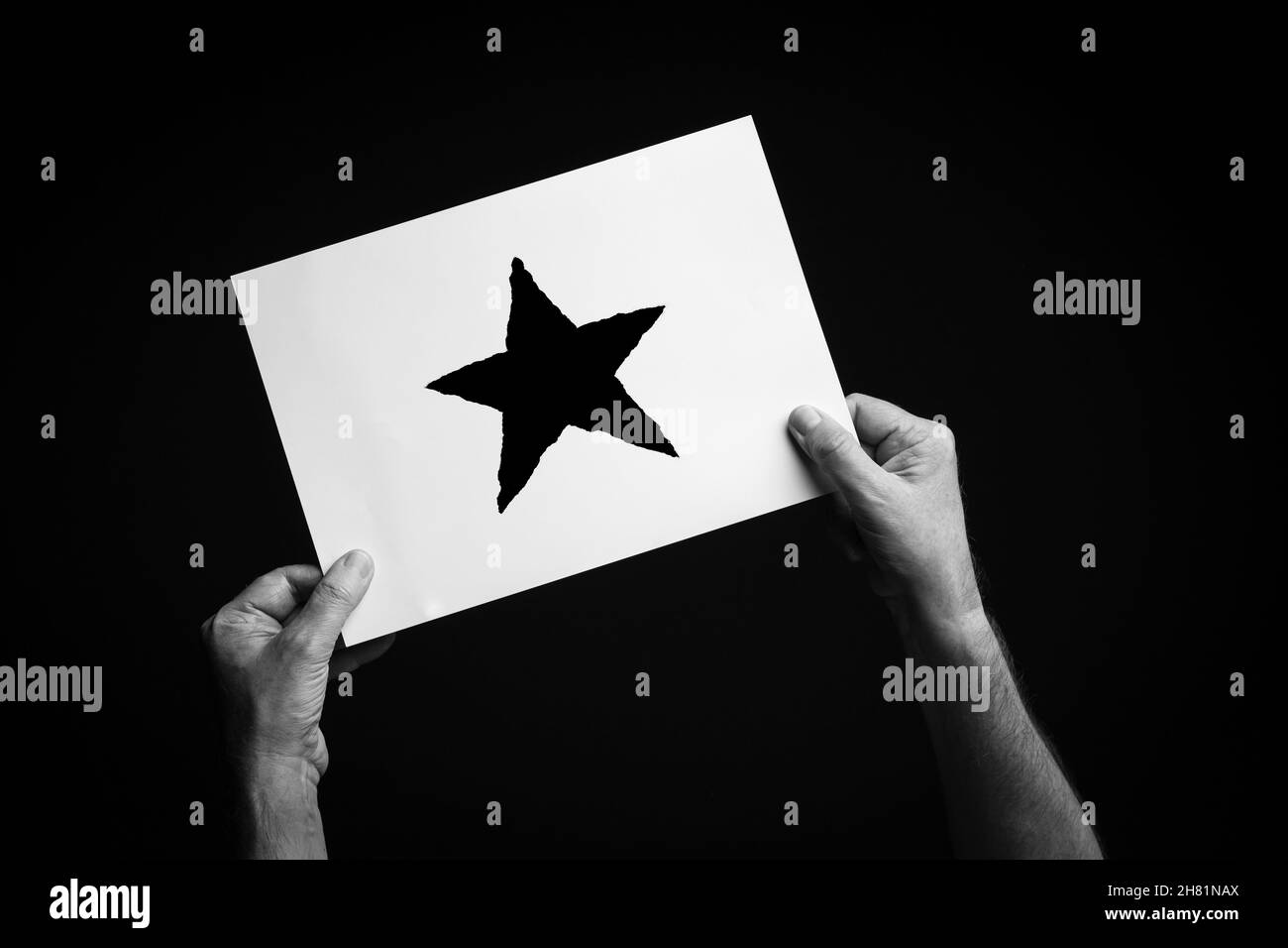 B+W image of male hands holding sheet of paper with christmas star symbol against black background. Stock Photo