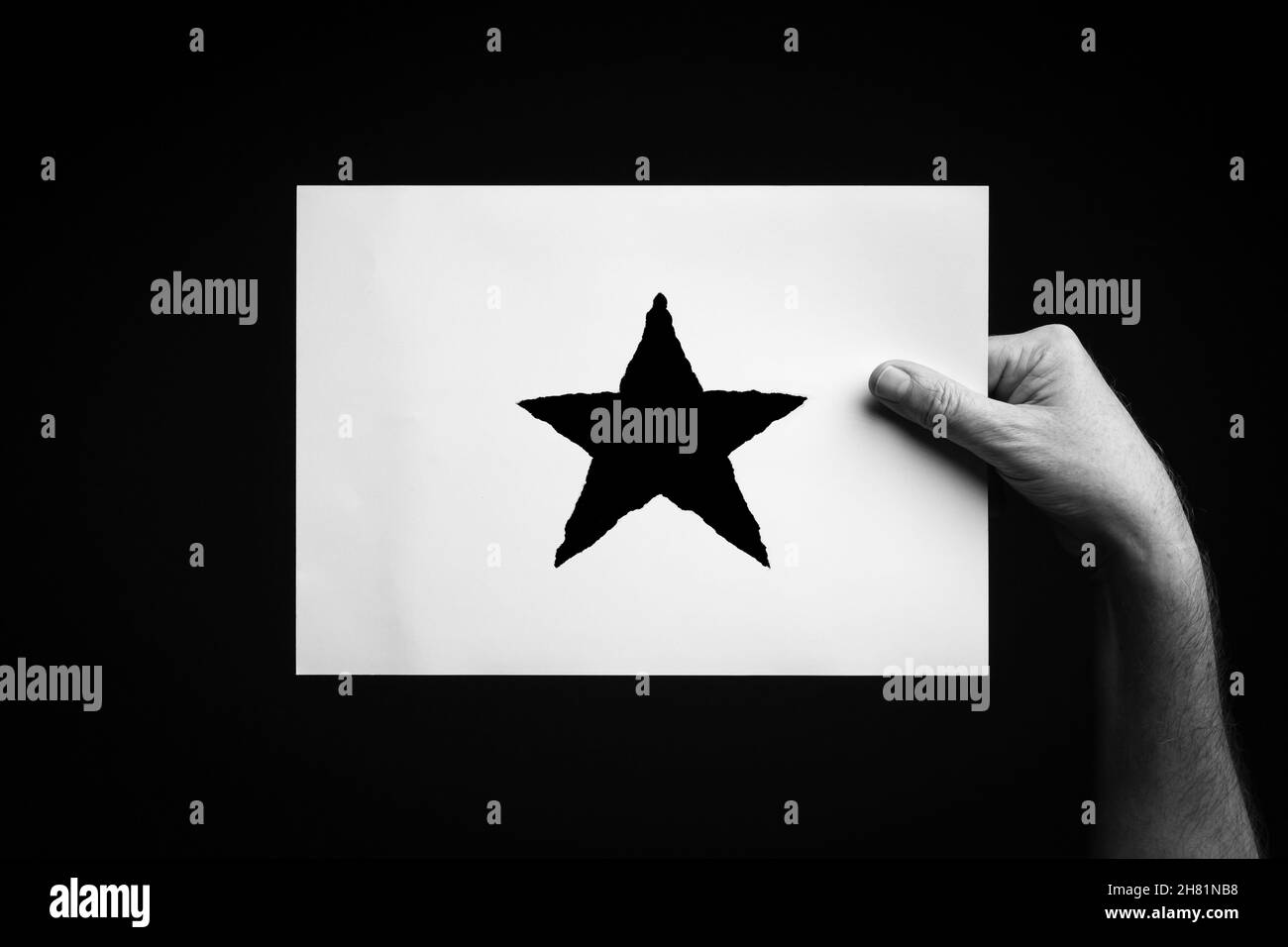 B+W image of male hand holding sheet of paper with christmas star symbol against black background. Stock Photo
