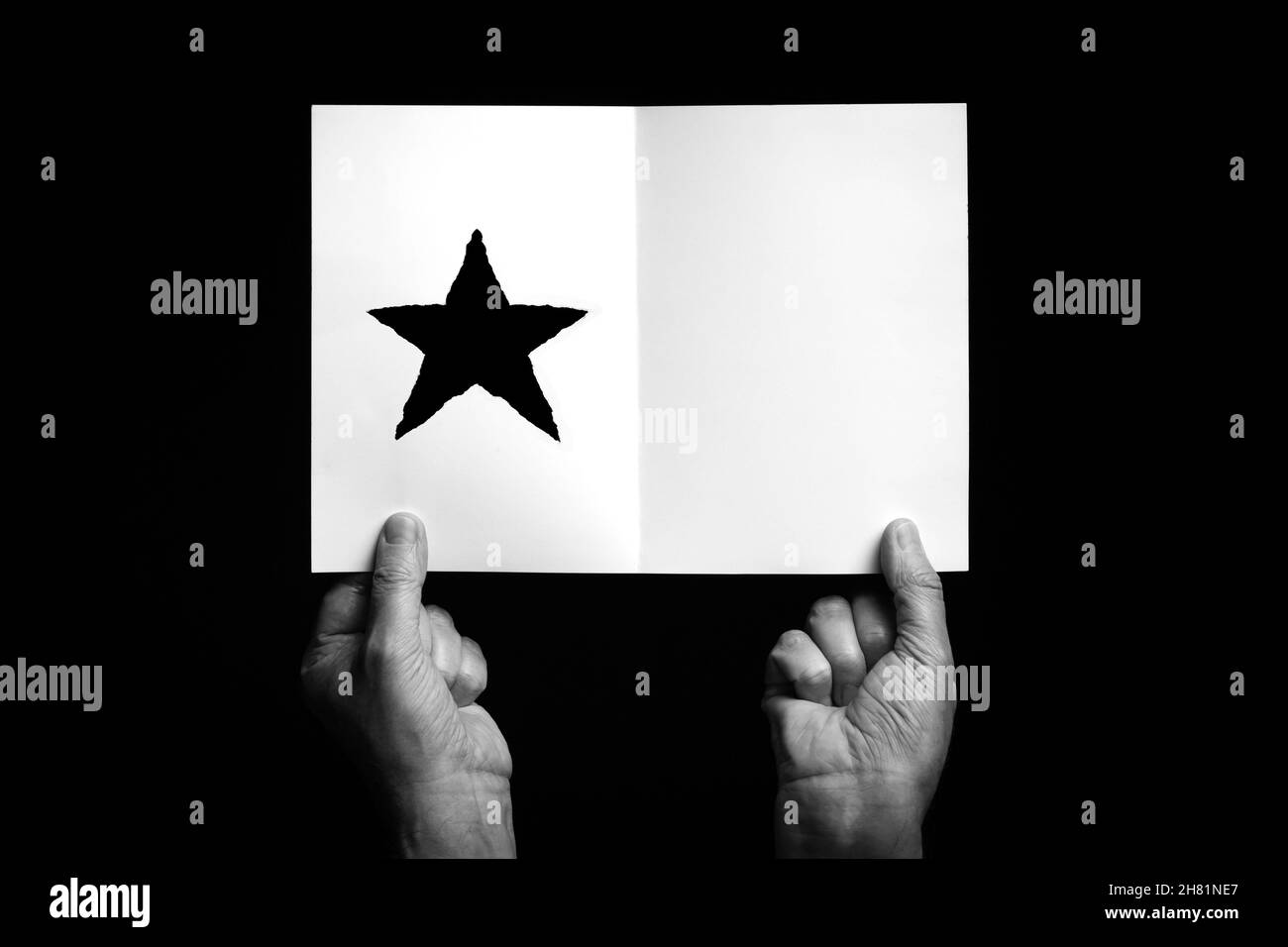 B+W image of male hands holding folded card with christmas star symbol against black background. Stock Photo