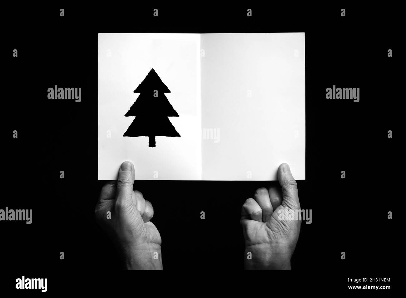 B+W image of male hand holding folded card with christmas star symbol against black background. Stock Photo