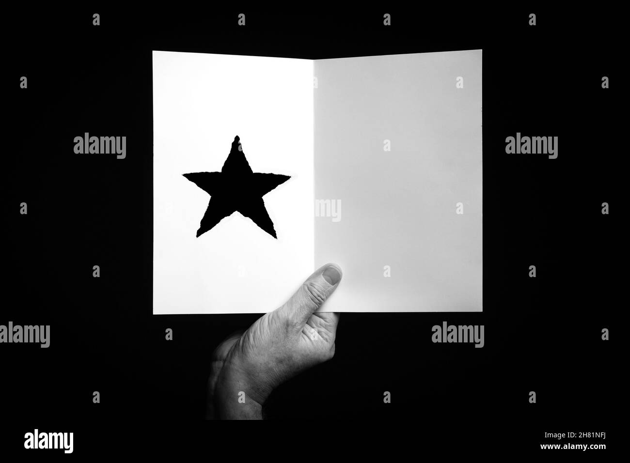 B+W image of male hand holding folded card with christmas star symbol against black background. Stock Photo