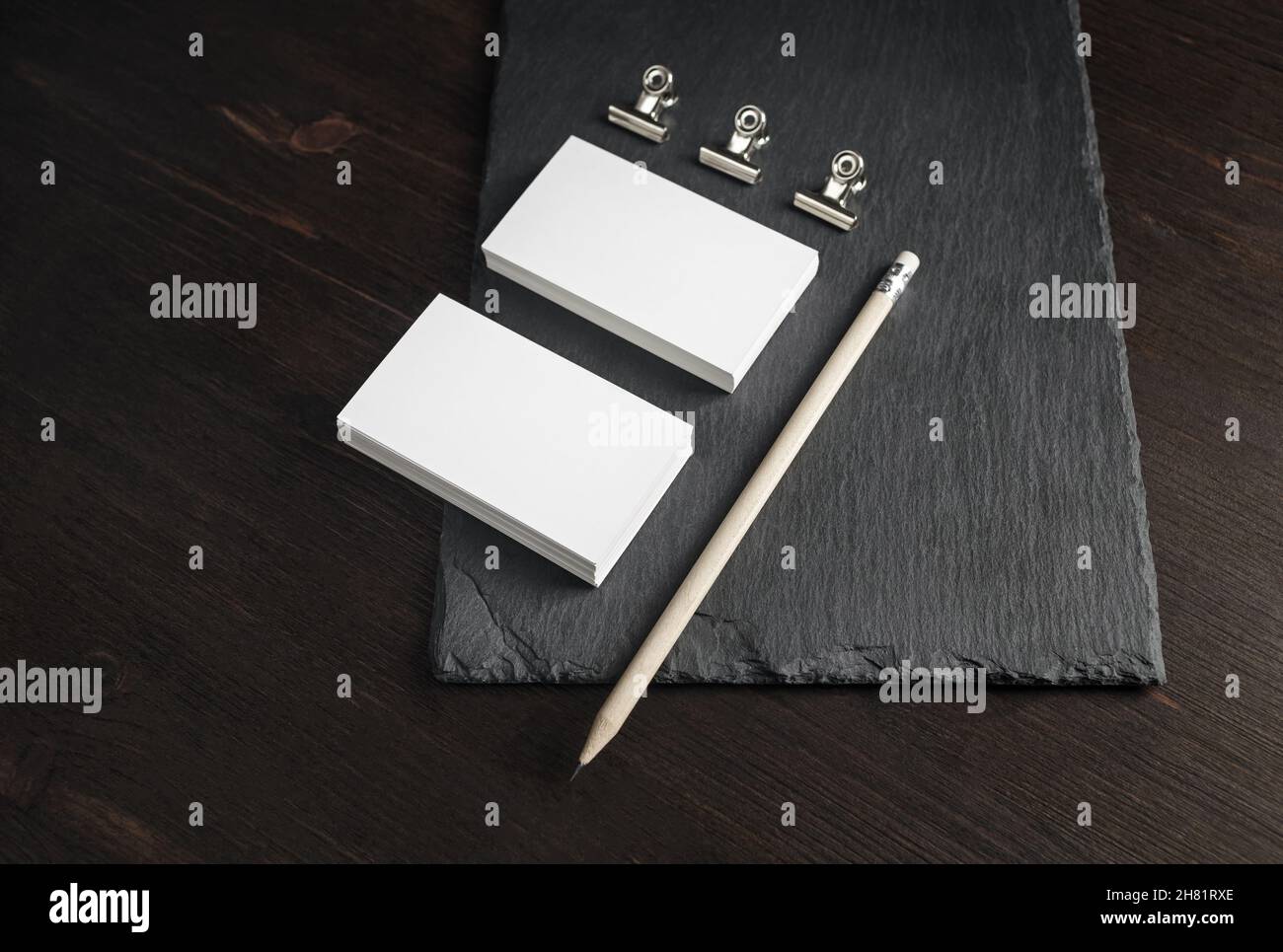 Two stacks of blank business cards, pencil and metal clamps on stone board background. Copy space. Stock Photo