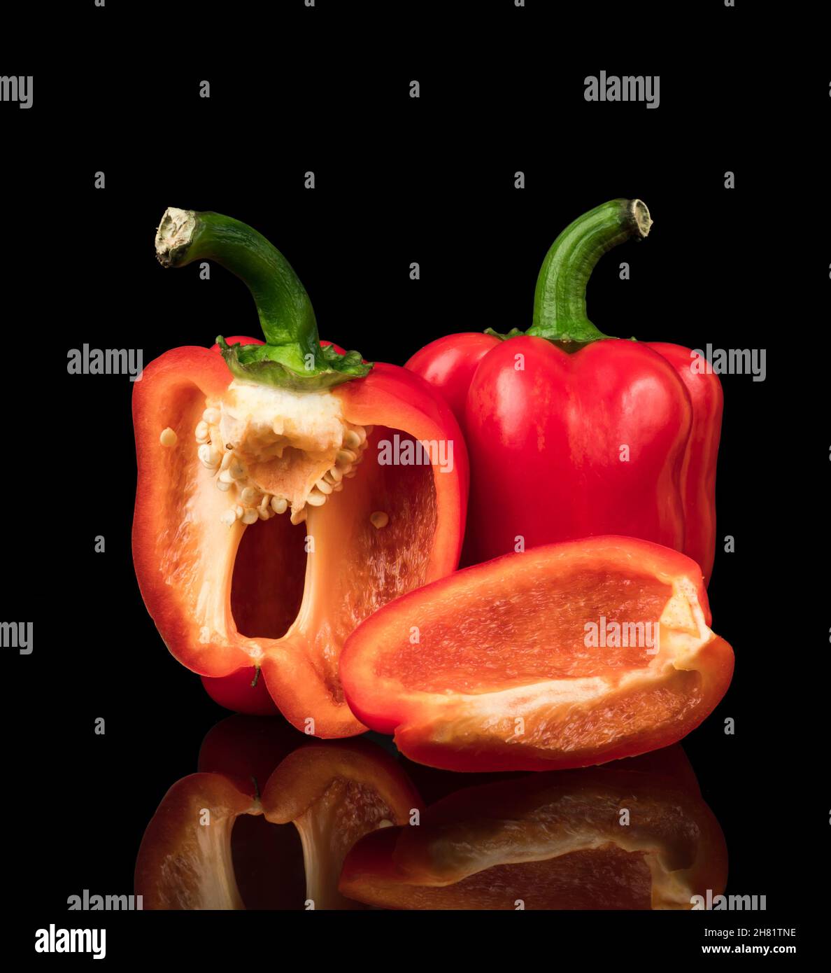 Sweet peppers, red, whole and cut into pieces, on a black background with reflection Stock Photo