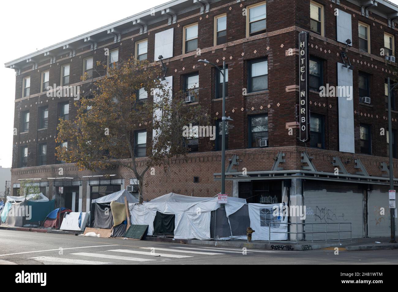Los Angeles, CA USA - November 20, 2021: Homeless tents line th sidewalk in front of an old run down hotel the Hotel Norbo on skid row Stock Photo