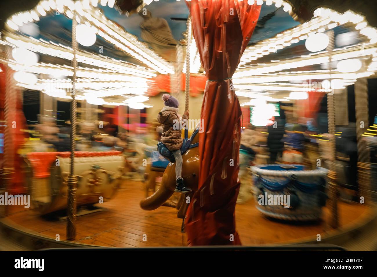 Panning image with a little girl riding a horse on a merry-go-round (carousel) during a cold winter night. Stock Photo