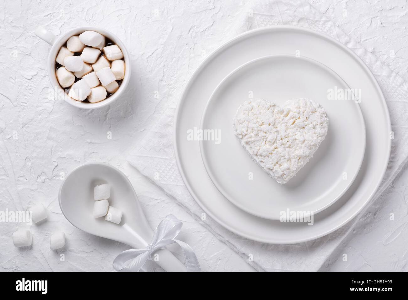 Heart shaped cottage cheese in a plate, coffee and marshmallows on a white table Stock Photo
