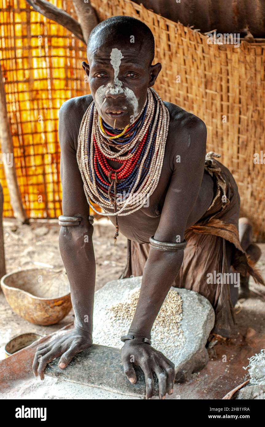woman in a hut grinding grain on a stone rock in Ethiopia from the Karo Tribe in the Omo Valley Stock Photo