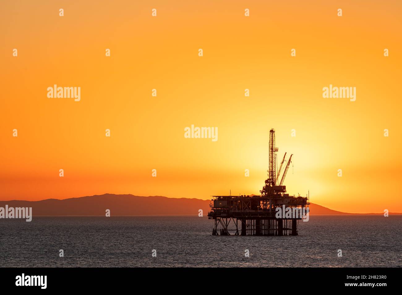 Offshore oil platform off the coast of California against a moody, orange sky as the sun sets behind the rig. Stock Photo