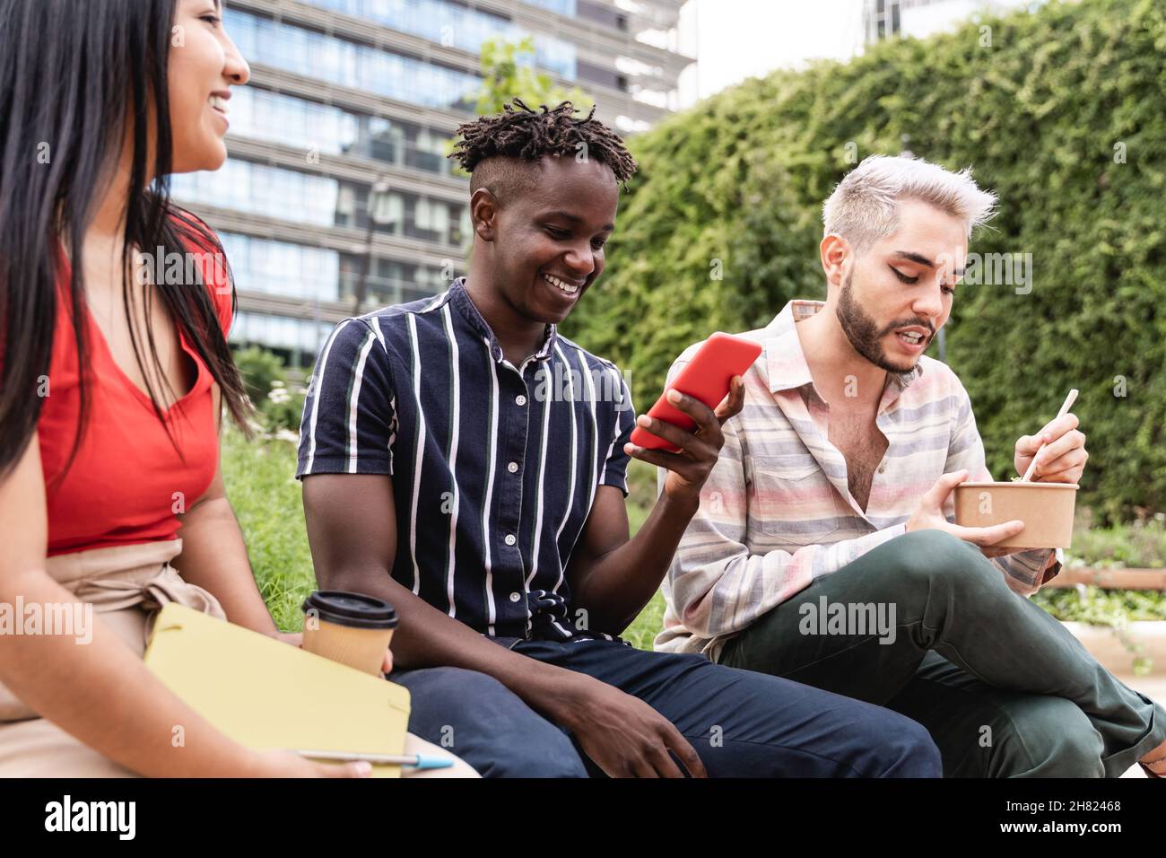 Diverse people having fun eating takeaway food outdoor in the city - Focus on non-binary man Stock Photo