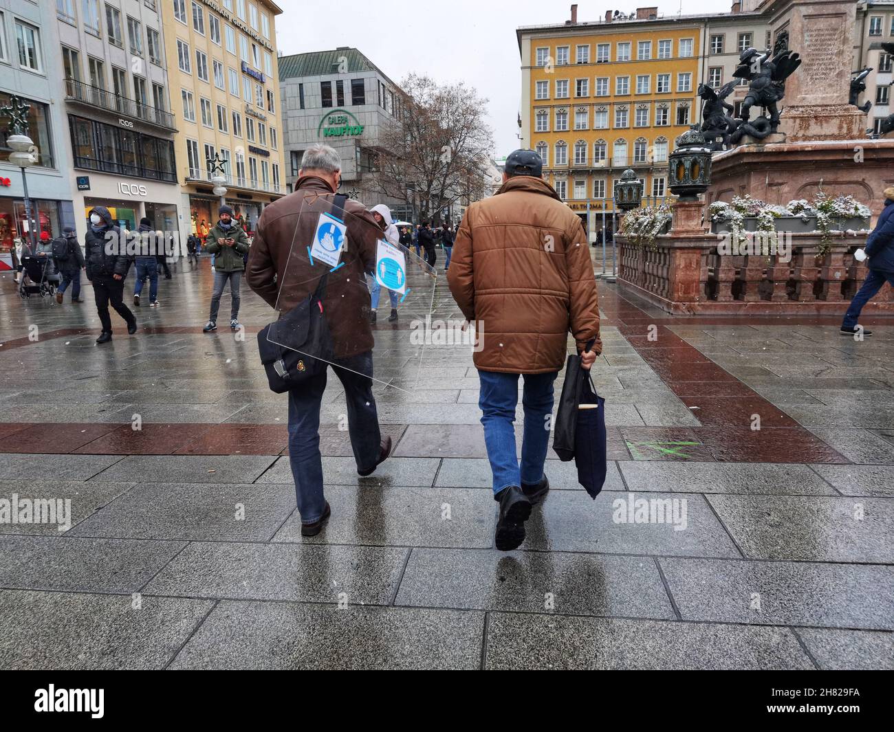 Munich, Bavaria, Germany. 26th Nov, 2021. A man in Munich, Germany carries a dividing glass across Marienplatz. Thr glass still has signs indicating it was used to slow or prevent the spread of Coronavirus. (Credit Image: © Sachelle Babbar/ZUMA Press Wire) Credit: ZUMA Press, Inc./Alamy Live News Stock Photo
