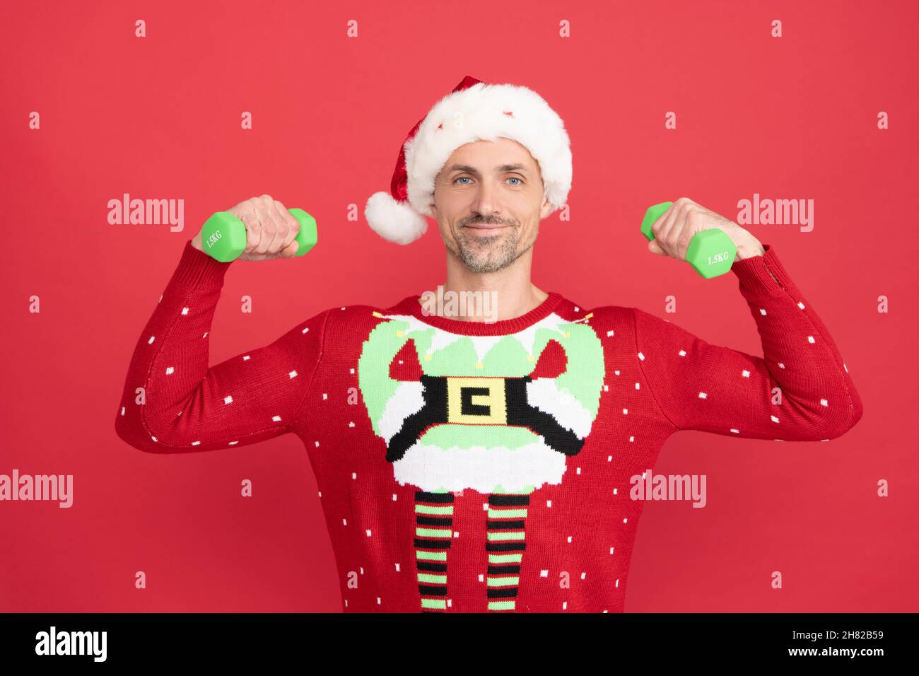 Happy Santa Claus man flex arms with hand weights doing dumbbell workout red background, Christmas Stock Photo