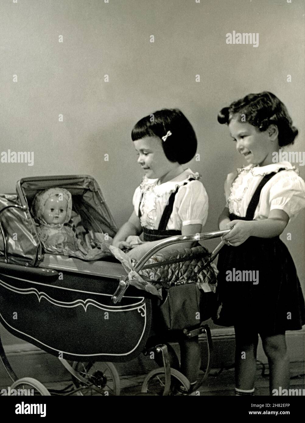 Two sisters playing with a baby carriage and a doll, circa 1951. Stock Photo