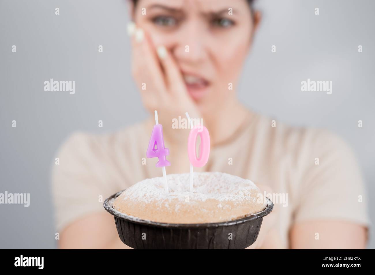 Unhappy woman holding a cake with candles for her 40th birthday. The girl cries about the loss of youth. Stock Photo