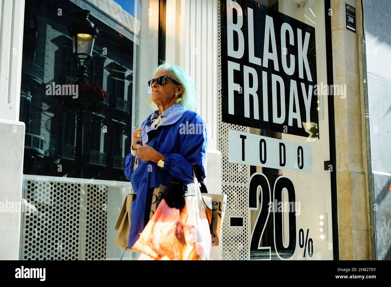 Malaga, Spain. 26th Nov, 2021. A woman carrying her shopping bags walks  past a Black Friday sale poster at a Bershka showcase in Malaga.In 2021,  online commerce has grown by 71% after