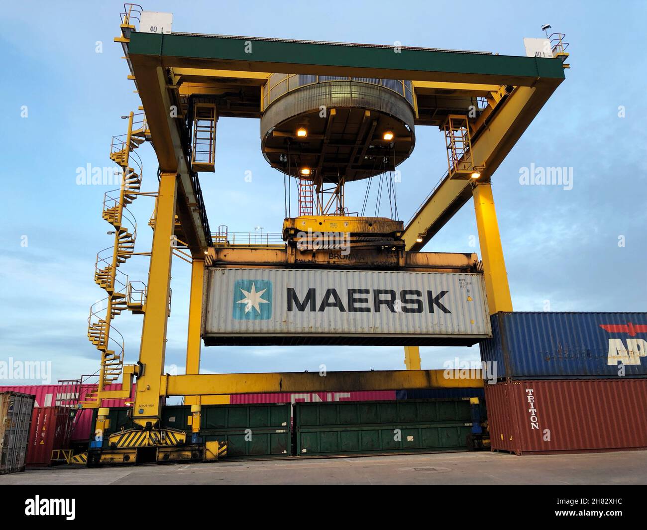 A Maersk shipping container being loaded onto a freight train by an overhead crane at a goods terminal or dock Stock Photo