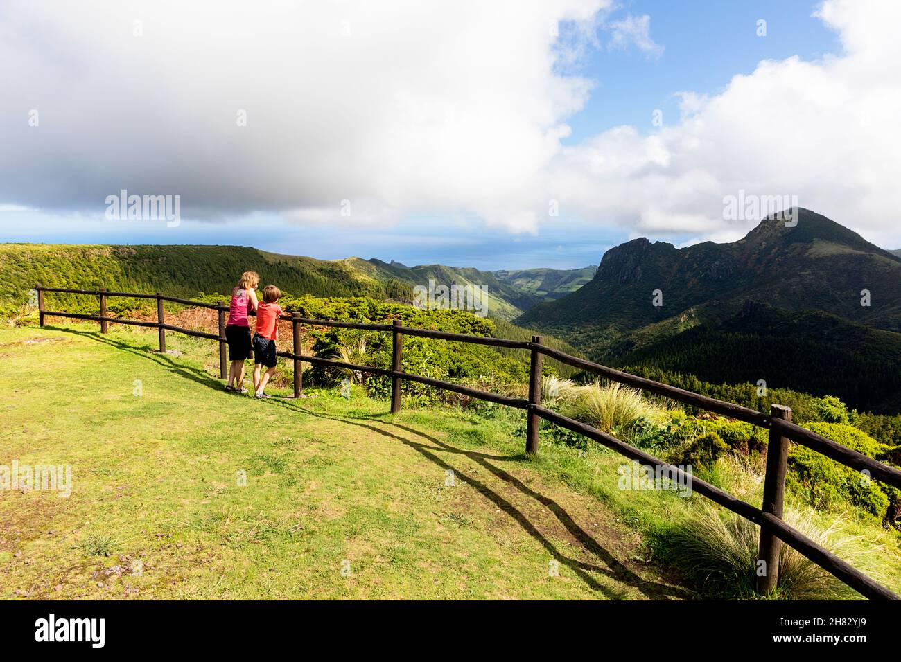 Mother and son leaning on wooden fence at viewpoint Miradouro do Vale da Fazenda viewpoint in Flores, Azores, Portugal Stock Photo