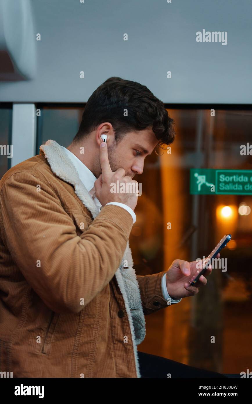 Side view of young male listening to songs in earbuds while riding bus in city at night Stock Photo