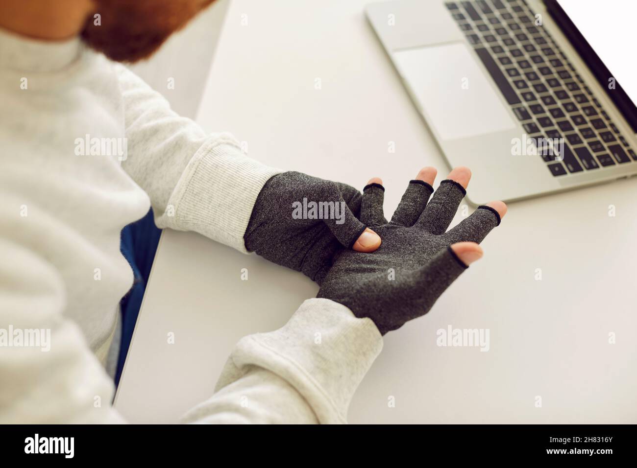 Man with rheumatoid arthritis wearing pain relief compression gloves while working on laptop Stock Photo