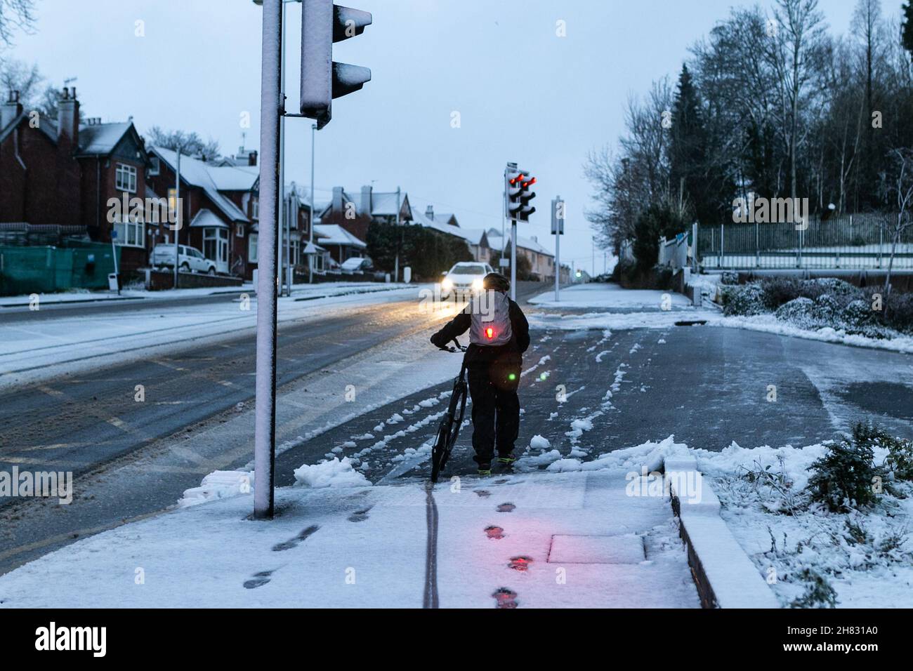 Cradley Heath, West Midlands, UK. 27th Nov, 2021. A lone cyclist decides to walk up the hill as a blanket of snow hits the the roads in Cradley Heath, West Midlands, as Saturday morning traffic is thanksfully light. Road conditions are dangerous. Credit: Peter Lopeman/Alamy Live News Stock Photo