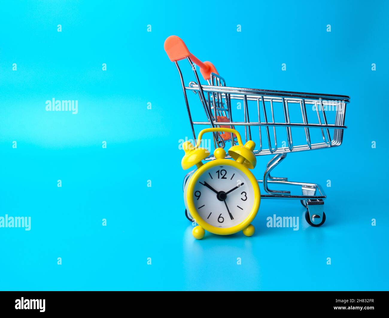 Shopping chart with alarm clock on a blue background with copy space