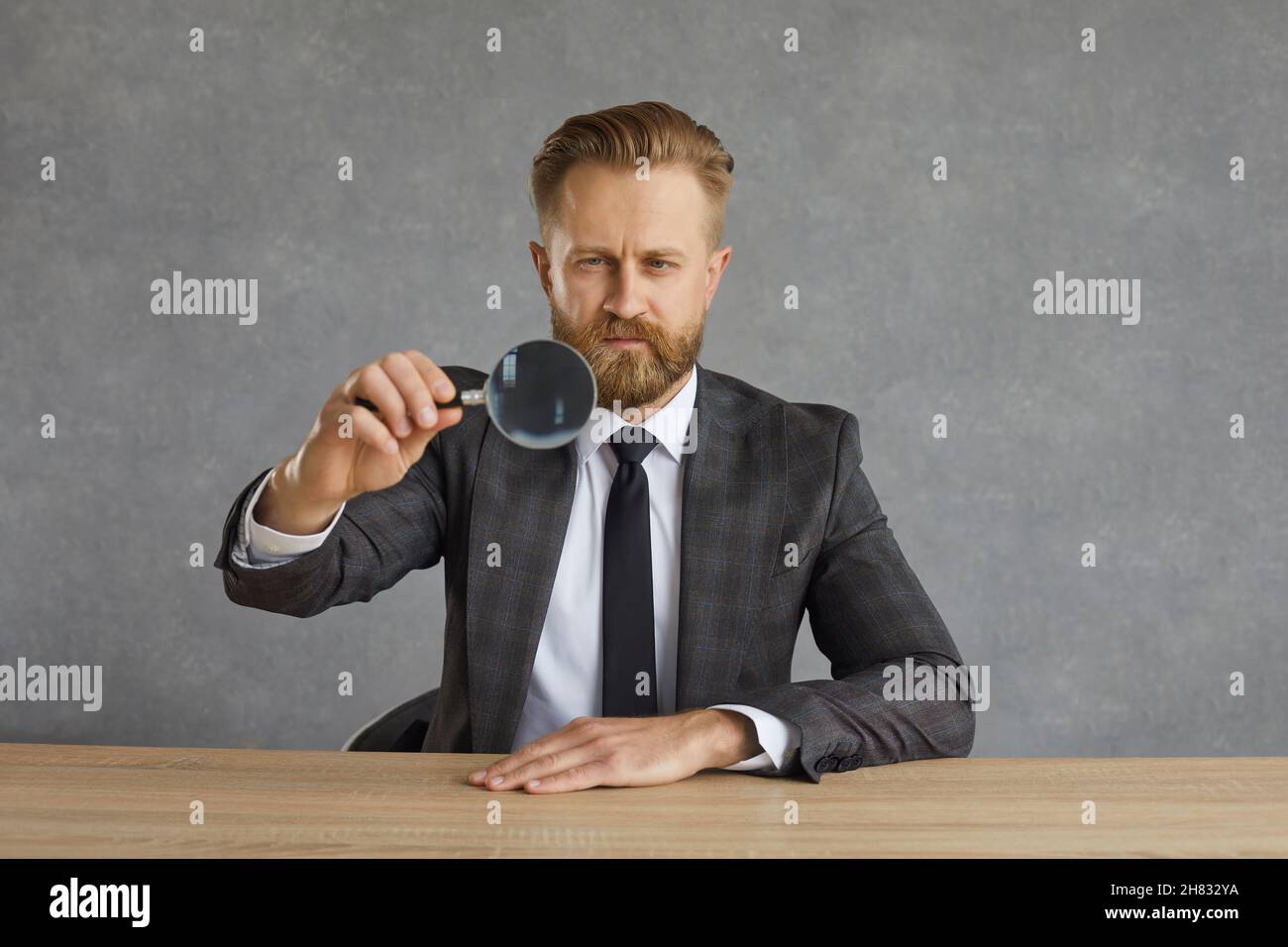 Serious focused businessman sitting at a table and looking through a magnifying glass. Stock Photo