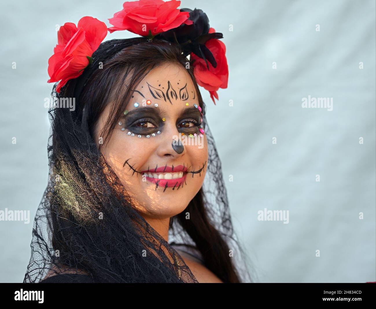 Cheerful positive optimistic young Mexican Yucatecan woman with traditional Catrina face makeup and glitter face jewels smiles on the Day of the Dead. Stock Photo