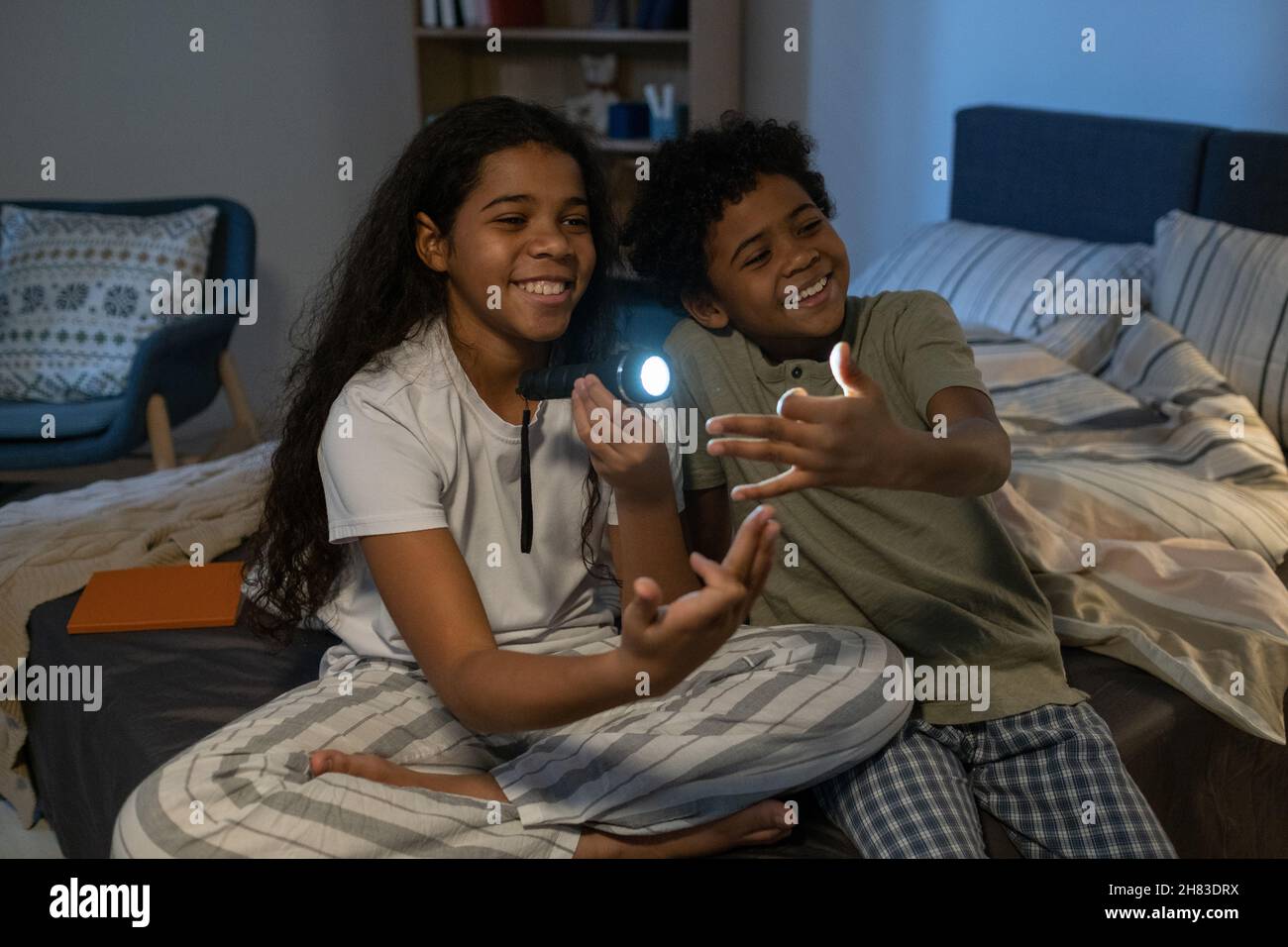 Cheerful African American siblings sitting on bed and gesturing hands ...