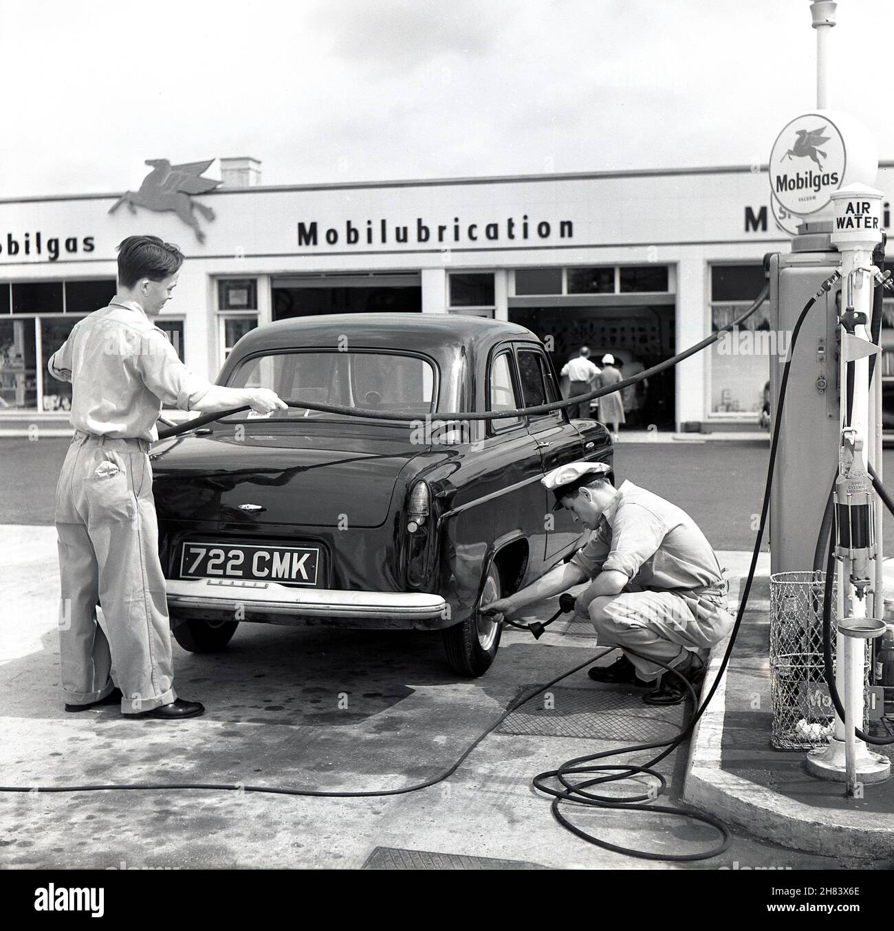 1950s, two uniformed forecourt staff at a new Mobilgas service station, beside an Austin car, one filling it with petrol and the other checking its tyre pressure, England, UK. An American oil company, Vacuum Oil trademarked 'Mobilgas' in 189. It merged with Socony in 1931 and in 1955 became the Socony Mobil Oil Company. Its first UK service stations opened in the early 1950s and were fully staffed with pump attendants and mechanics. Motor car sales grew significantly in the post war years and Britain became the second-largest manufacturer of cars in the World after the USA. Stock Photo