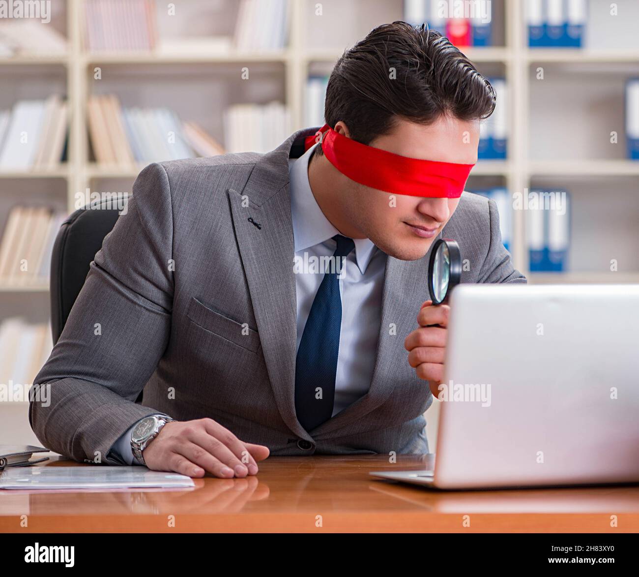 the-blindfold-businessman-sitting-at-desk-in-office-2H83XY0.jpg