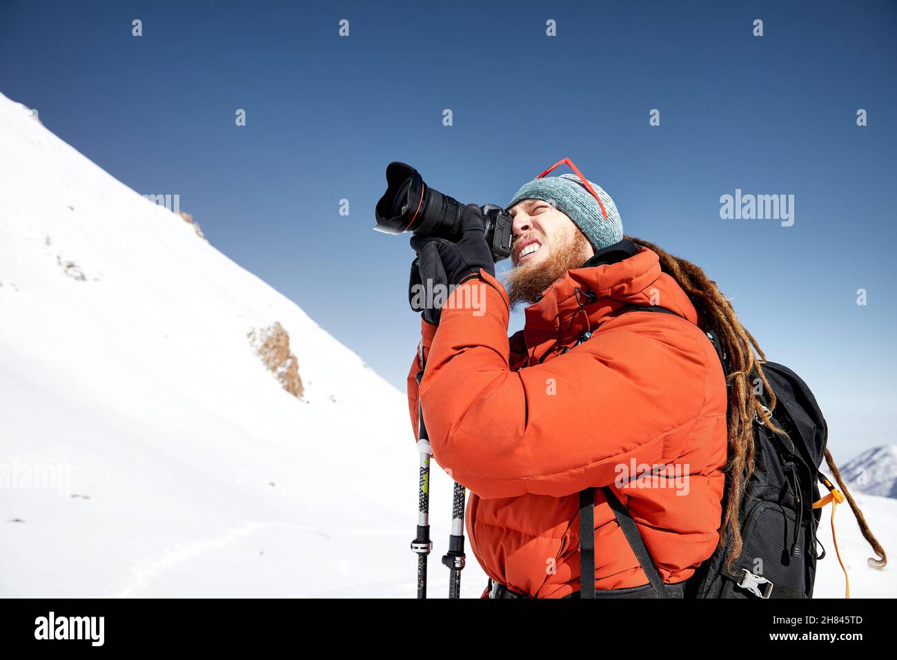 Photographer with camera taking a picture in red jacket at the snow mountains against blue sky in Almaty, Kazakhstan Stock Photo