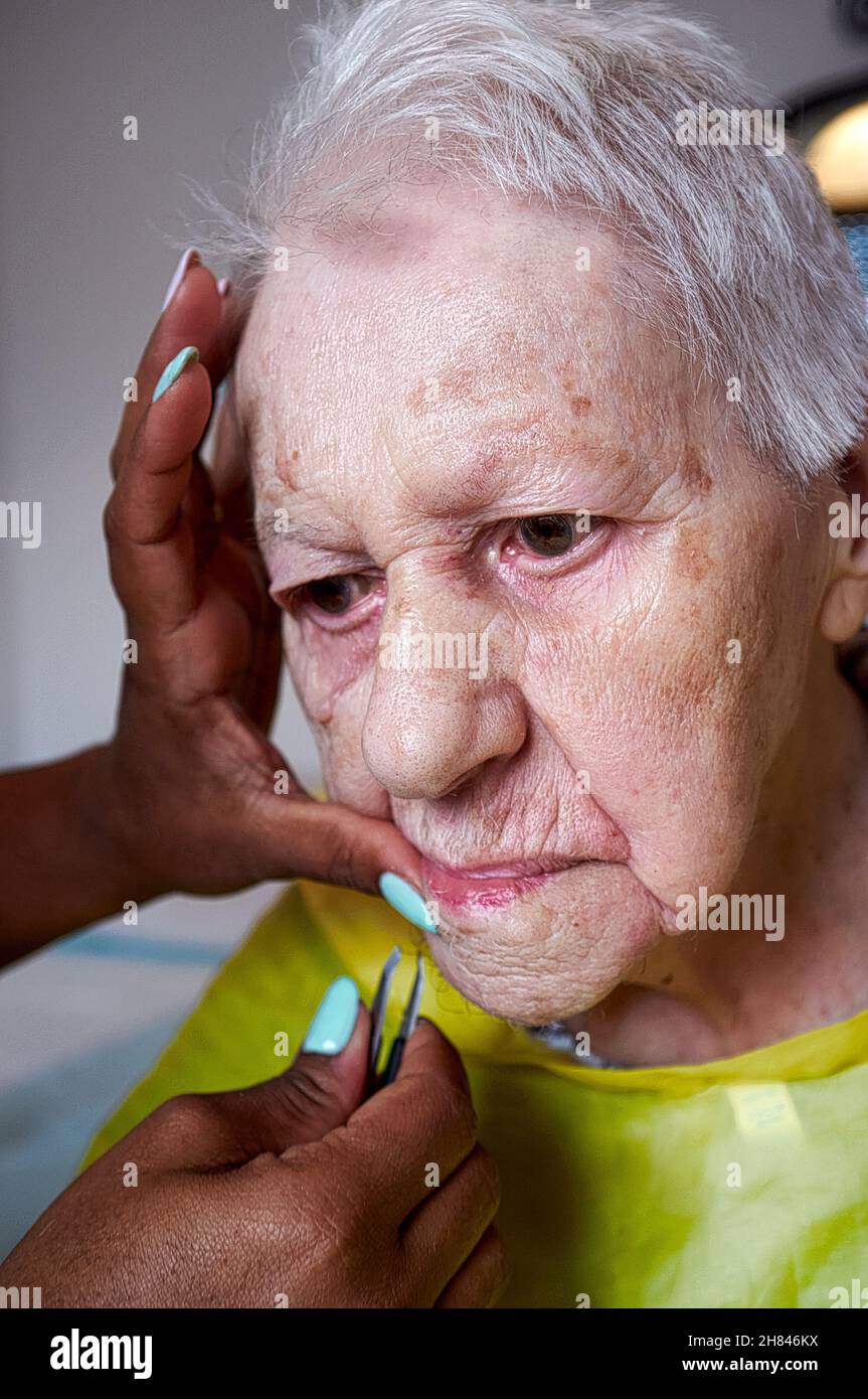elderly woman receiving facial hair removal from african american