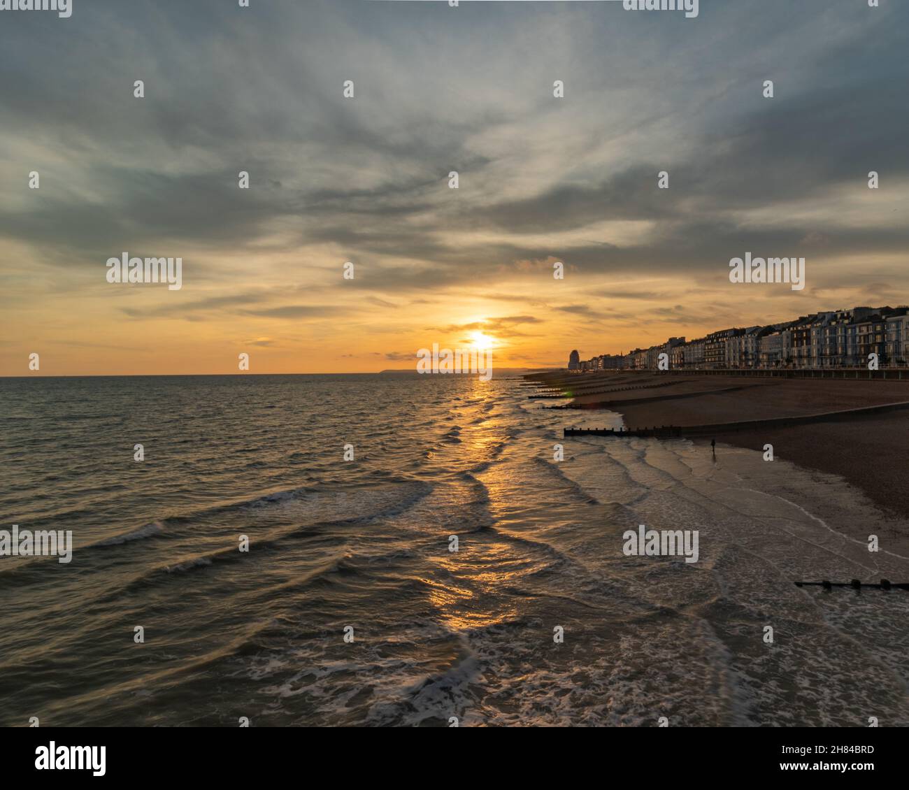 Sunset and golden hour on Hastings Pier, England, Uk looking out towards Eastbourne with the sea and the groynes in the foreground.Promenade Stock Photo