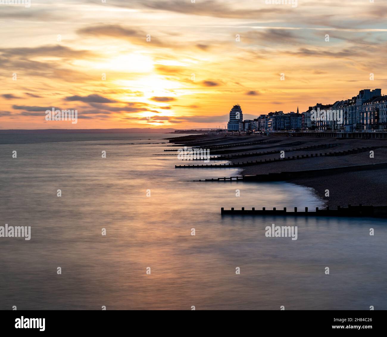 Sunset and golden hour on Hastings Pier, England, Uk looking out towards Eastbourne with the sea and the groynes in the foreground.Promenade Stock Photo