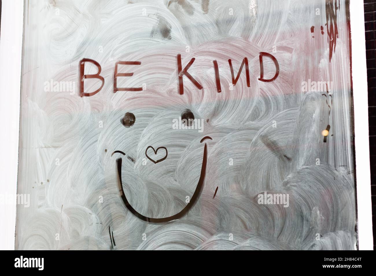 'Be kind' with a smiley face and love heart drawn into white wash on a empty shop window to spread some love and positivity during the pandemic Stock Photo