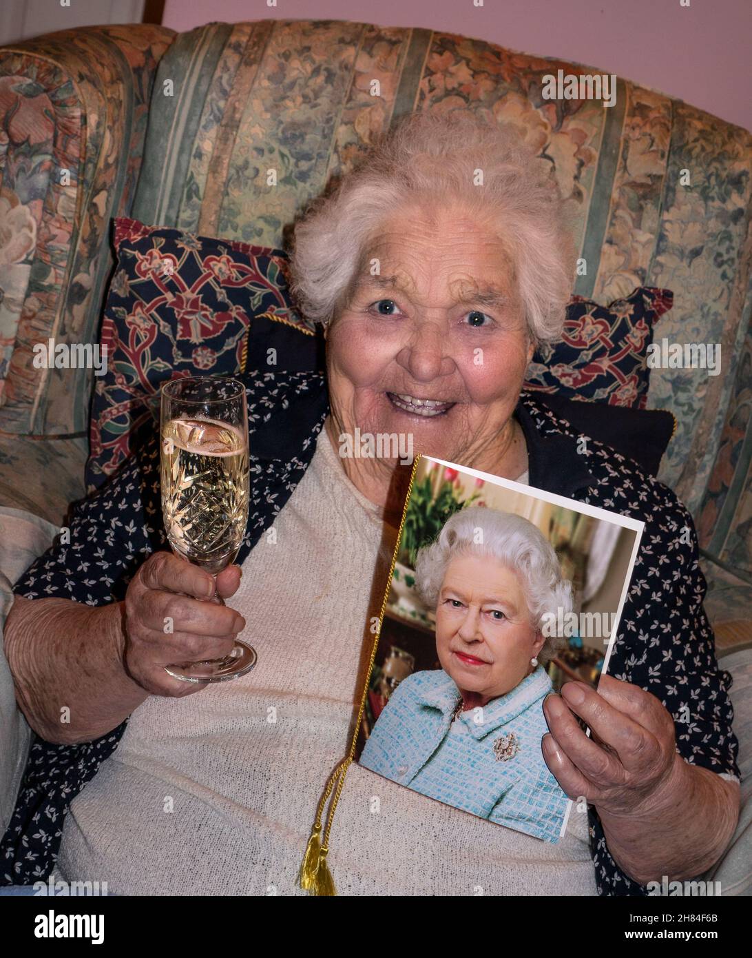 100 years of age happy alert lady birthday celebration smiling bright alert lady holding a celebratory glass of champagne and THE '100' years of age traditional customary congratulatory birthday card from HM The Queen UK Stock Photo