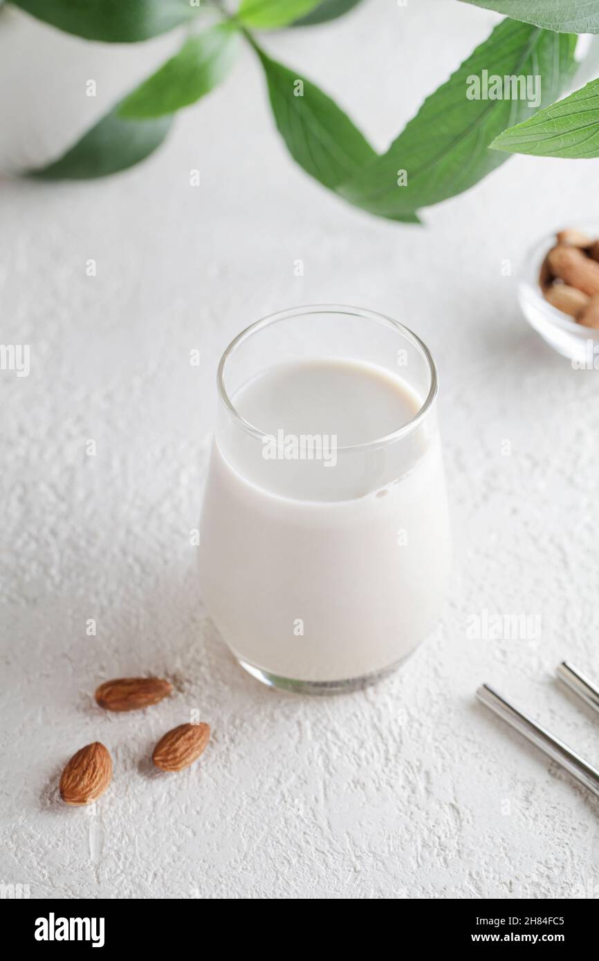 Vegan almond milk in glass with nuts and green plant on white background. Healthy vegetarian food. selective focus. Non dairy alternative milk Stock Photo