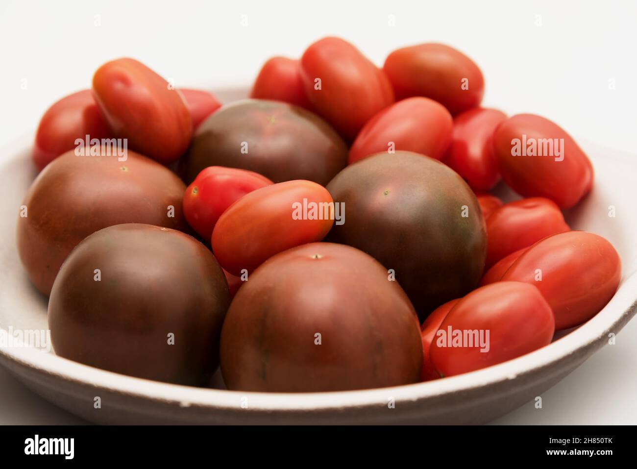 Delicious kumato and cherry tomatoes piled on a clay plate over white