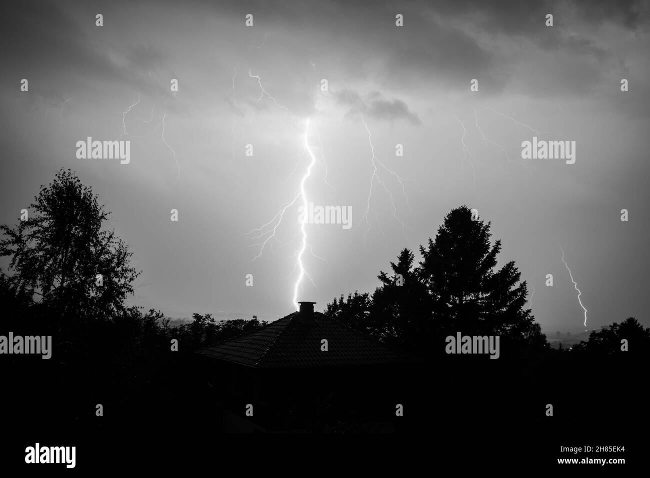 Black and white lightning bolt strike over a house and forest in Bulgaria. Beautiful powerful dark storm. High quality photo Stock Photo