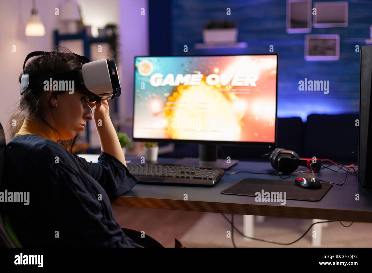Gamer using vr goggles to play video games and losing on computer. Person playing online game with controller on monitor and virtual reality glasses. Adult with gaming equipment. Stock Photo