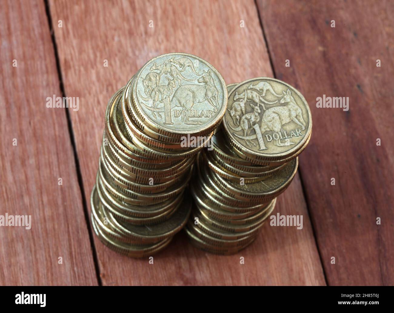 Two piles of Australian one dollar coins on a wooden background. Shallow depth of field focus. Stock Photo