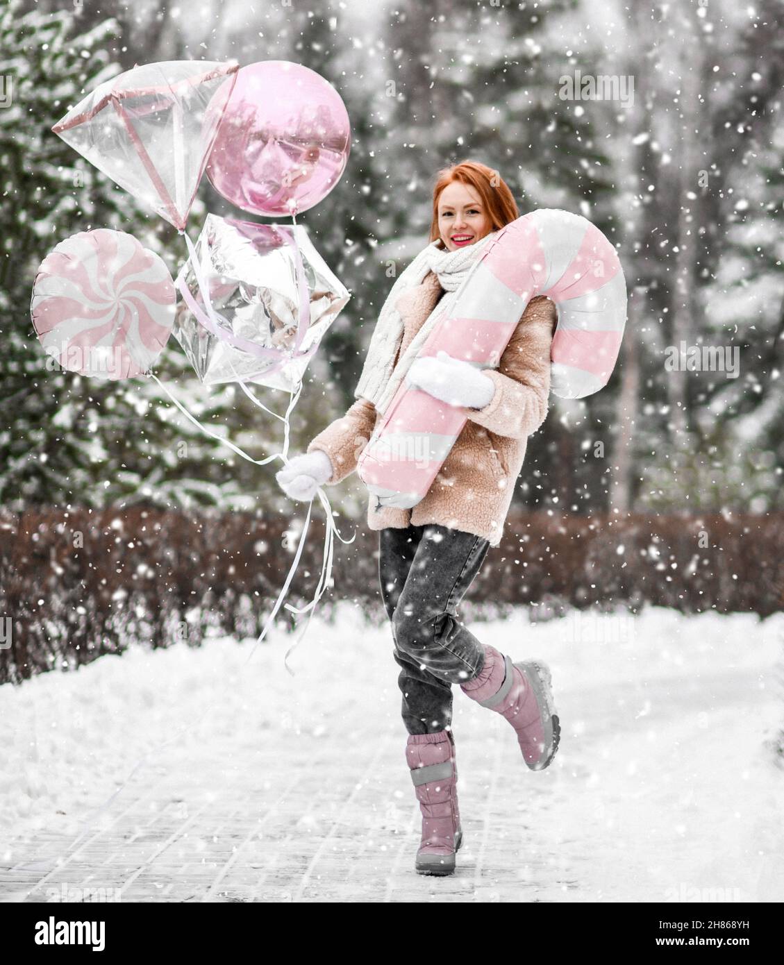 Girl walking outside under snow with pink balloons near winter forest. Happy red hair woman celebrate birthday Stock Photo