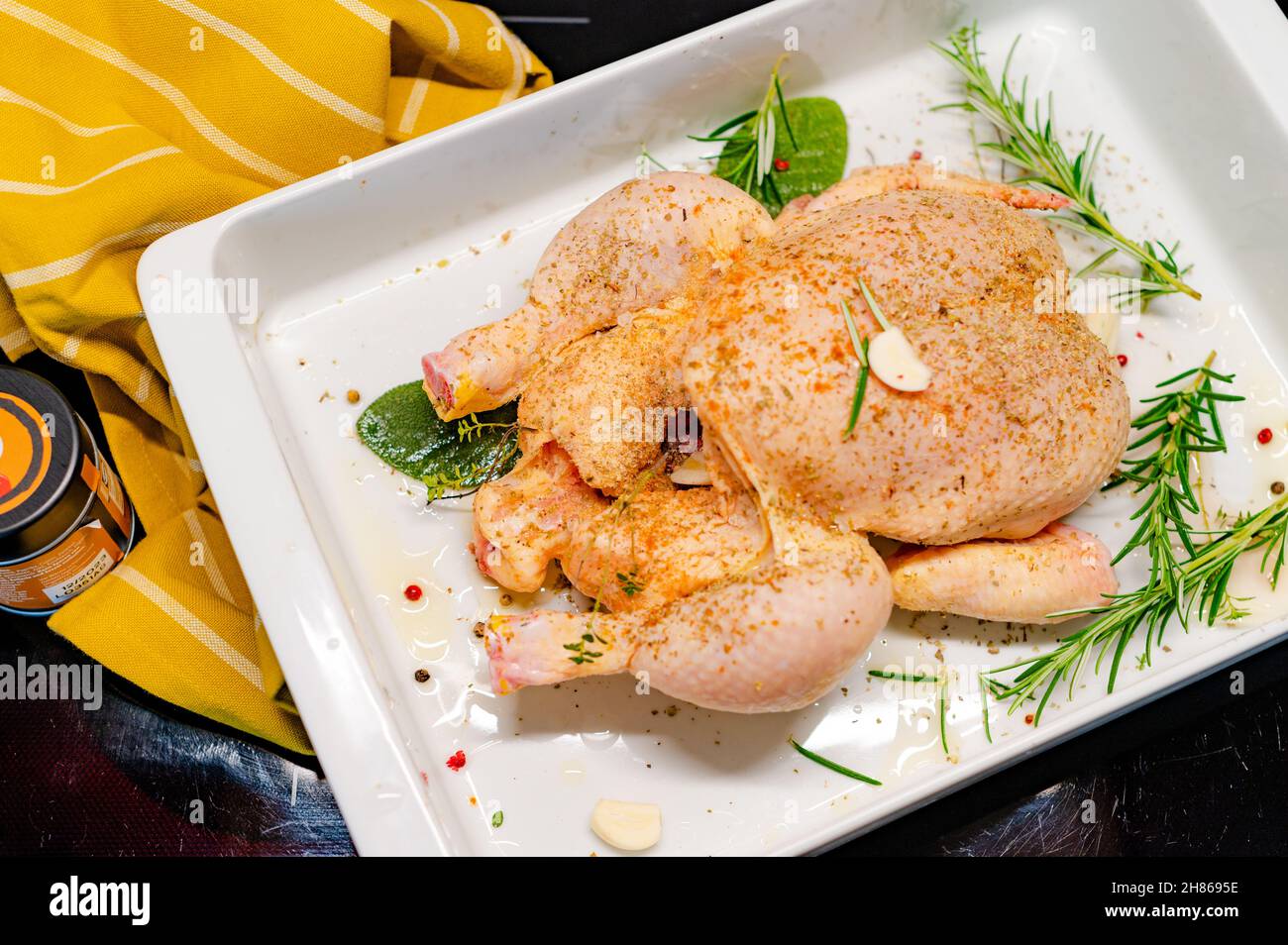 A whole dressed chicken with herbs spices in a white tray ready for
