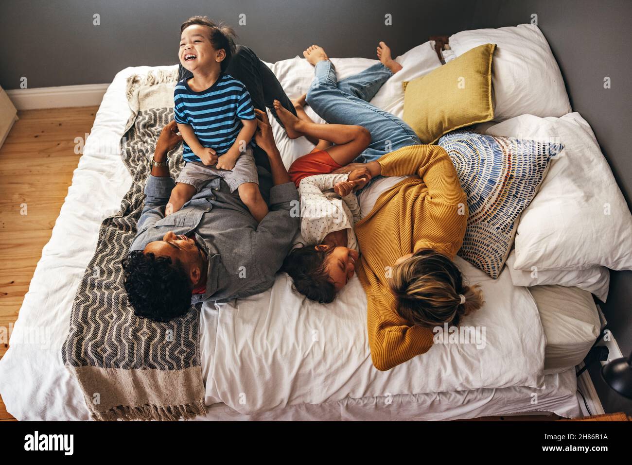 Top view of parents playing with their children while lying on the bed. Happy family laughing and having fun together on the weekend. Mom and dad spen Stock Photo