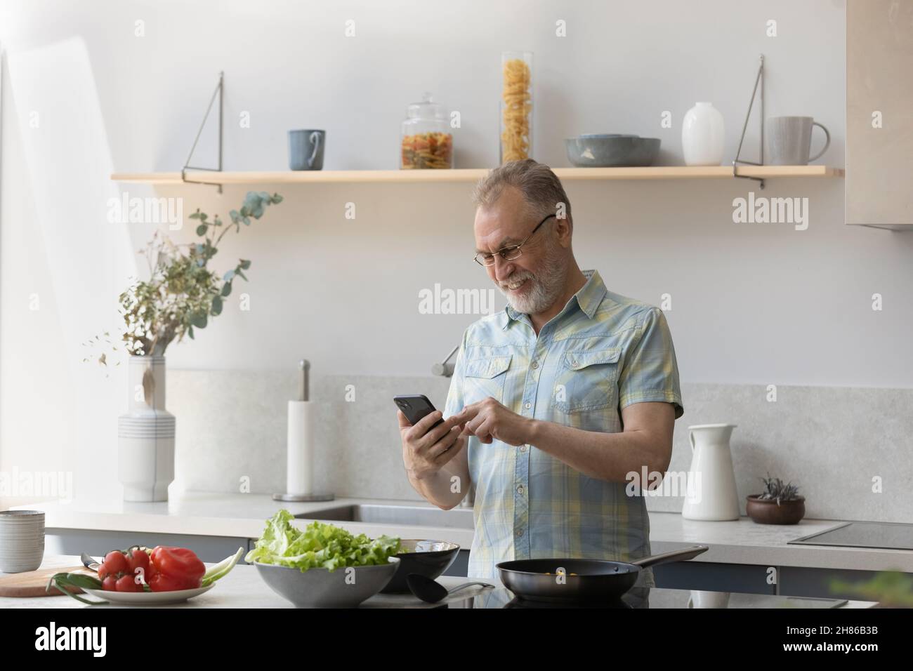 Cheerful older homeowner man consulting internet on smartphone Stock Photo